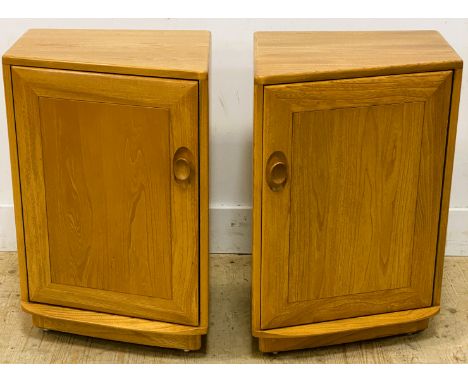 A pair of Ercol elm side cabinets, of trapeze shape, with a cupboard door enclosing a shelf, standing on a plinth base, 68.5c