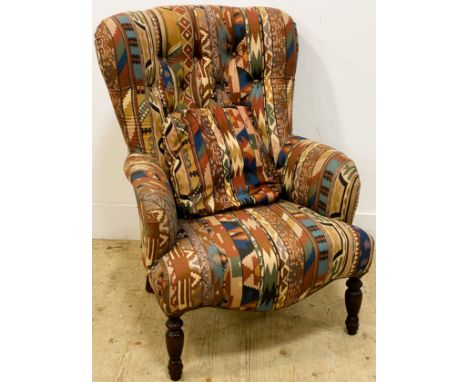 A Victorian style armchair, with a shaped button back and padded arms above a shaped stuffover seat, standing on turned front