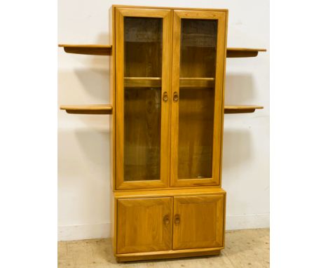 An Ercol elm display cabinet, with a pair of glass doors enclosing shelves, with two pairs of slot on shaped shelves either s