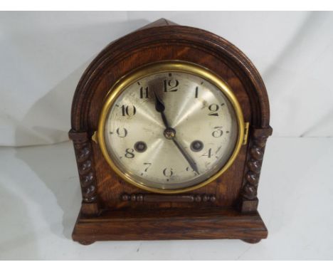 An oak cased mantel clock, Jacobean style decoration, silvered dial with Arabic numerals behind glazed brass bezel, hour and 