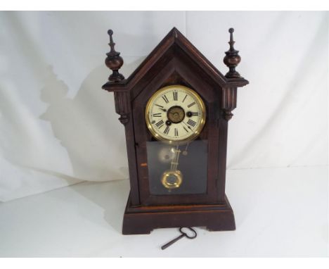 A small kitchen steeple clock, timepiece with alarm, the case having two turned finials, grid-iron styled pendulum Estimate £