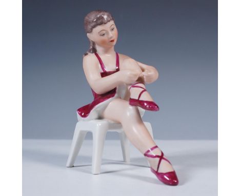 Charming hand-painted porcelain figurine depicting a ballerina seated on a white stool as she ties the ribbon of her ballet s