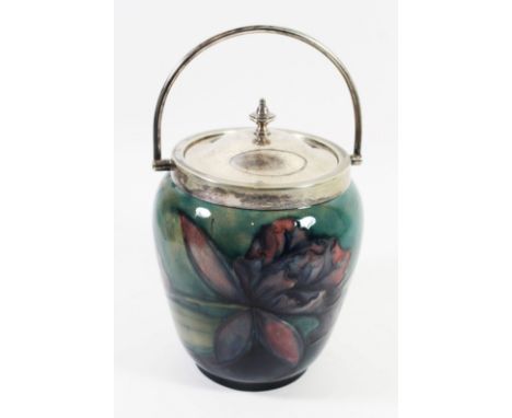 A William Moorcroft biscuit barrel with silver-plated rim and coverDecorated in the Purple Orchid pattern on a light green gr