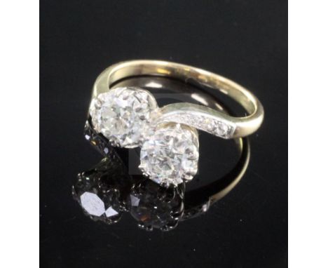 A gold and platinum, two stone diamond cross over ring, with diamond set shoulders, each large diamond weighing approximately