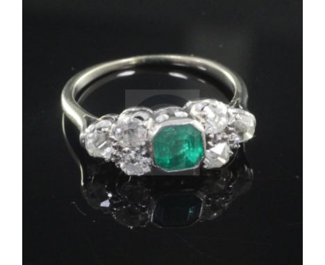 A mid 20th century white gold, emerald and diamond dress ring, the central emerald flanked by six old round cut diamonds, siz