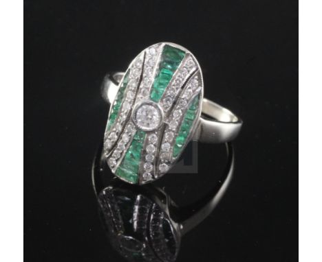 An Art Deco style 18ct white gold, emerald and diamond oval dress ring, set with round cut diamonds and fancy cut emeralds,