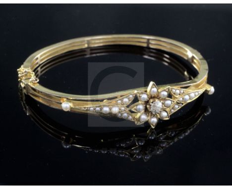 A late Victorian high carat gold, diamond and seed pearl set hinged bangle, of pierced flower head design.