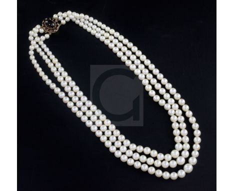 A triple strand graduated cultured pearl necklace with garnet cluster set oval gold clasp, 60cm.