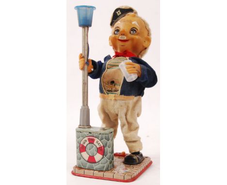 A vintage tinplate battery operated figure ' Down The Hatch .' In the form of a tipsy sailor stood holding a lamp post. With 