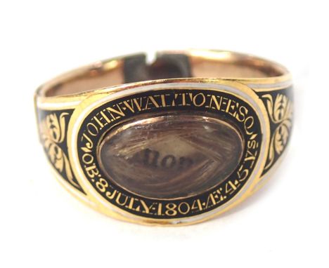 A Victorian memorial ring, with oval panel holding locket of hair, on a black enamel border marked John Walton Esquire, born 