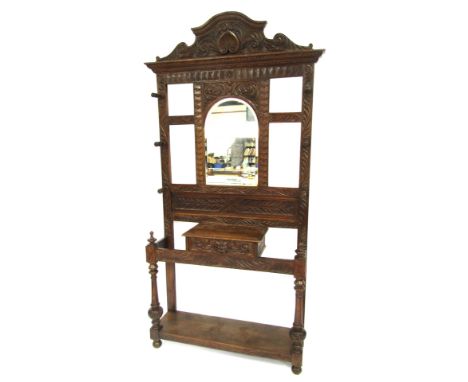 An early 20thC carved oak hall stand, the scroll leaf and shell carved top above an arched mirrored and central panel with si