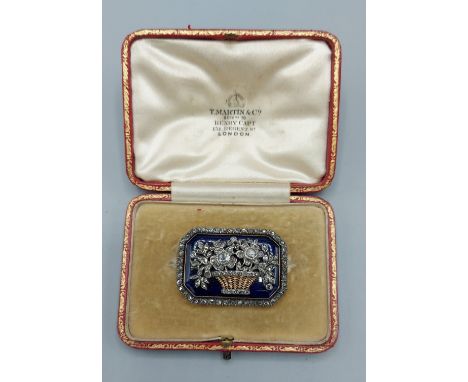 An Edwardian gold brooch in the form of a basket of flowers set with Diamonds on an enamel panel and surrounded by Diamonds, 