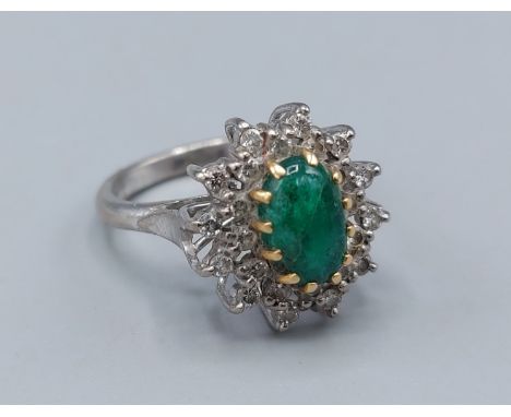 An 18ct white gold Emerald and Diamond cluster ring, with an oval Cabochon Emerald surrounded by Diamonds, 5.9gms, ring size 