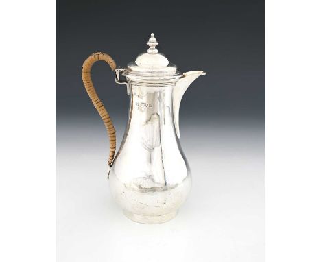A George V silver hot water jug, of bellied cylindrical form with rattan-covered handle, the stepped domed hinged cover with 