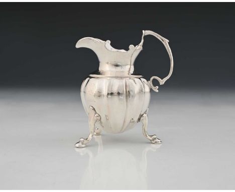 A George II silver cast cream jug, the fluted ovoid body raised on three scroll and hoof feet with faceted trefoil junctions,