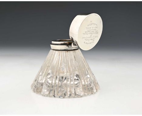 An Edwardian silver-mounted glass desk top inkwell, the spreading fluted glass body with hinged silver cap, presentation insc