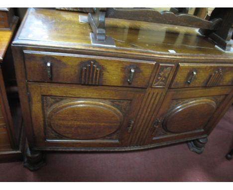 A 1930's Oak Bow Fronted Sideboard, with a mirror back, two short drawers, over cupboard doors, with roundels, on cup cover s