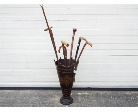 An umbrella / stick stand with a quantity of walking sticks including one with silver collar and handle in the form of a hors