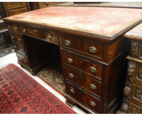 An early 20th Century mahogany knee hole desk, the tooled leather insert top over three frieze drawers (one bearing retailers