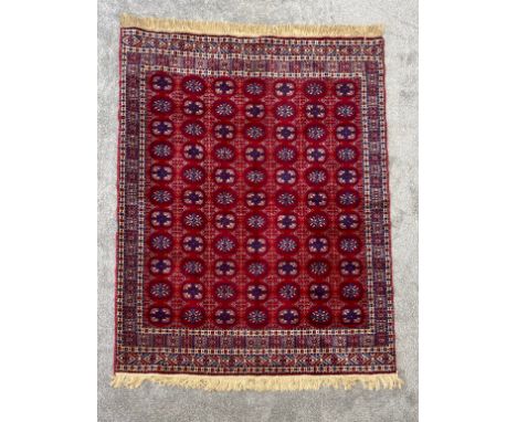 A silk Turkoman carpet with repeating flowerhead motifs on a burgundy field within stylised multiple borders. L.194 W.141cm