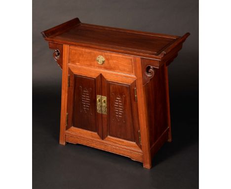 A Chinese hardwood altar cabinet, rectangular top with scroll ends above a drawer and a pair of doors, carved in relief with 