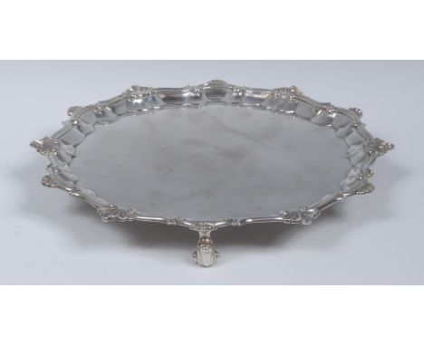 A George II silver shaped circular salver, fluted shell and S-scroll border, plain field, wrapped knurl feet, 33cm diam, Will