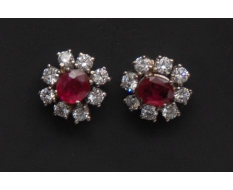 A pair of ruby and diamond flower head earrings, each with a central cushion cut ruby surrounded by eight round cut diamond p