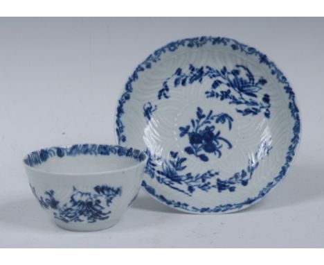 A Worcester tea bowl and saucer, in relief with feathered mouldings, decorated in underglaze blue with flowers and sprigs, wo