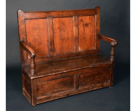 An 18th century pine vernacular box settle, three-panel back, downswept arms with turned supports, planked set with sliding c