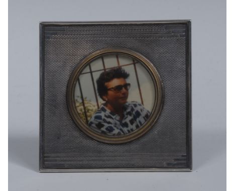 An Art Deco silver square easel timepiece frame, circular aperture, geometric borders on an engine turned ground, 9cm wide, T