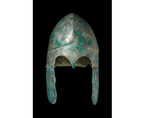 Ca. 500-300 BC.A bronze helmet forged in one piece, featuring high-arched eyebrows with a nose guard and a flaring neck guard