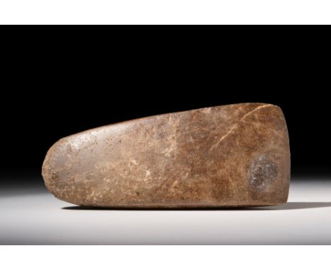 Ca. 3500 - 2000 BC.A Neolithic highly polished axe head in brown stone. The axe is trapezoid in shape with a curved blade and