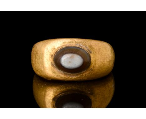 Ca. AD 100-300.A gold finger ring composed of a rounded hoop and expanding shoulders. The oval bezel is set with a convex ova