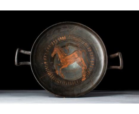 Ca. 5th century BC.A black-glazed terracotta kylix featuring a shallow bowl with a short foot and raised handles that extend 