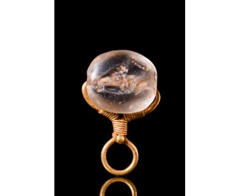 Ca. 600-400 BC.A gold pendant of a loop design, decorated with fine gold wire coils and a granule; holding a rock crystal sca
