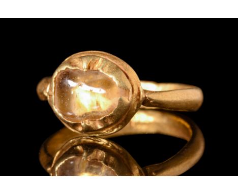 Ca. AD 800.A gold finger ring formed of a slender round hoop that supports a large bezel set with a rock crystal gem. Size: D