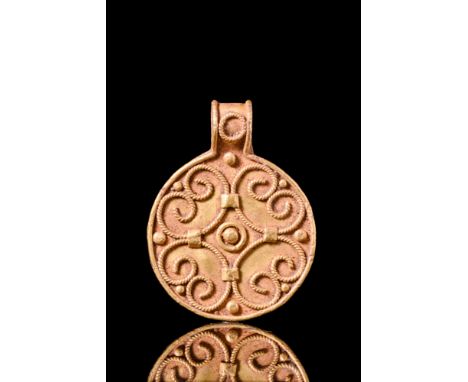 Ca. AD 900-1100.A gold Viking bracteate pendant with a raised border and thick suspension loop adorned with a small applied c