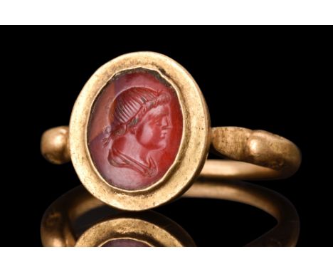 Ca. AD 300.A gold finger ring featuring a rounded hoop with duck-head finials. The bezel is set with a carnelian intaglio dep