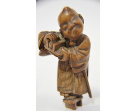 Japanese wood netsuke carved as a sage standing on one foot and holding his other shoe, height 2"