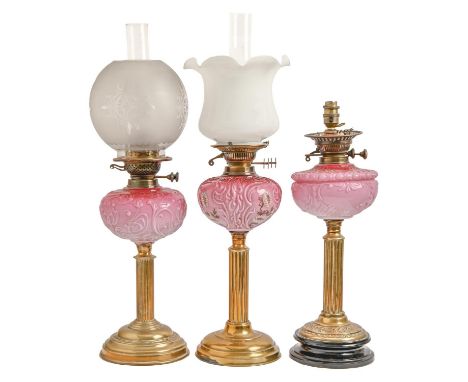 Three Victorian brass oil lamps,&nbsp; of columnar form, each with scroll moulded pink glass fount (one enamelled) and brass 