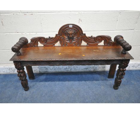 AN EARLY 20TH CENTURY OAK GOTHIC HALL BENCH, with turned armrests, scrolled backrest, with a central mask, repeating carved d