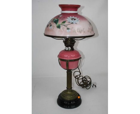 A Victorian brass pedestal oil lamp having pink tinted milk glass shade decorated with flowers above a pink glass font on a f