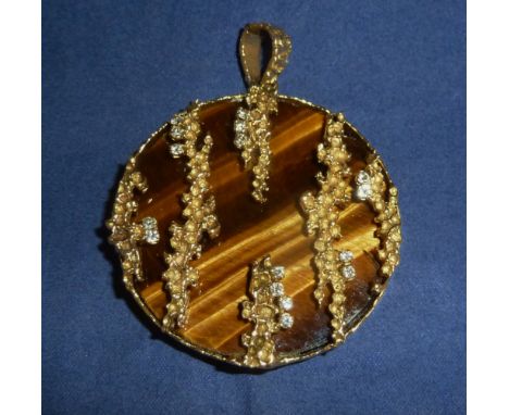 A modernist large circular tiger's eye pendant, the yellow metal trailing pierced mounts set with 16 diamonds, London 1972, m