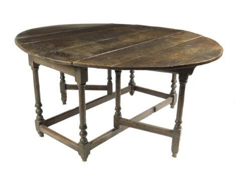  A mid 17th century oak gateleg table, the oval drop-leaf top on turned column and bobbin supports united by peripheral stret