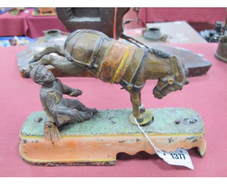 A Cold Painted Cast Iron Moneybox, modelled in the form of a bucking mule, beside a boy holding a stick on an oval base, with