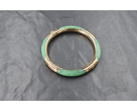 A Chinese jade and yellow metal hinged bangle having engraved decoration, and concealed clasp, safety chain missing and damag