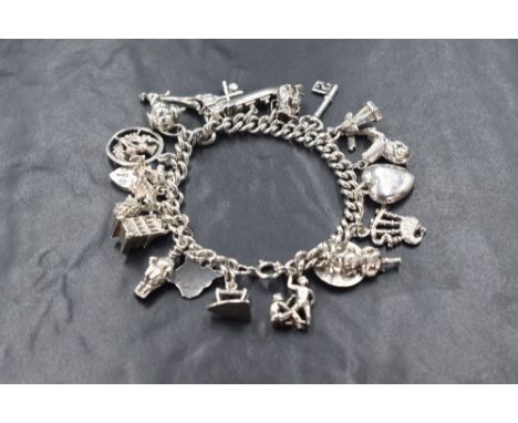 A white metal charm bracelet having twenty one charms bagpipes, leek etc, approximately 69.5g