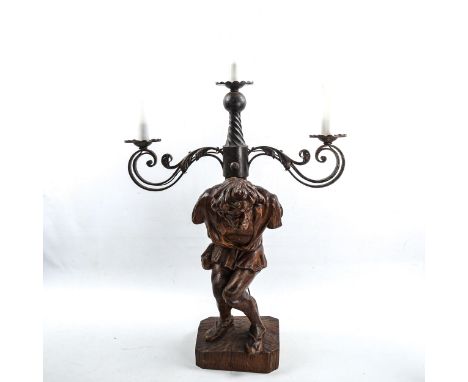 An unusual wrought-iron 3-branch lamp, supported by a carved wood figure of the Quasimodo, height to top of figure 45cm, over