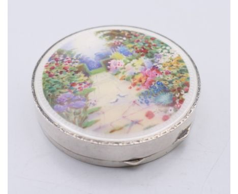 An early 20th century silver and enamel compact, the lid decorated with a floral garden scene.  6 cm diameter. 