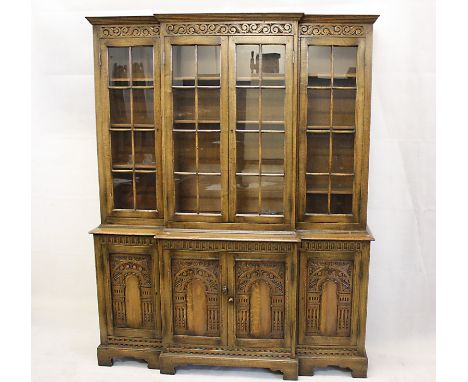 A reproduction oak elevated breakfront bookcase, the four panel glazed doors to shelved interior over carved panel doors to b